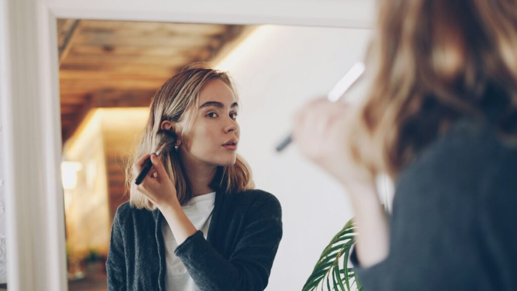 Young woman applying makeup in mirror